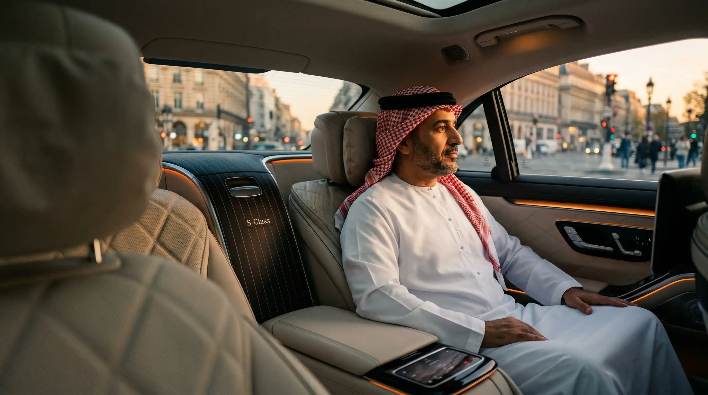 Distinguished passenger in the rear cabin of a Dahab Mercedes S-Class, private driver in suit visible in reflection, light leather interior, Parisian boulevard at sunset in the background